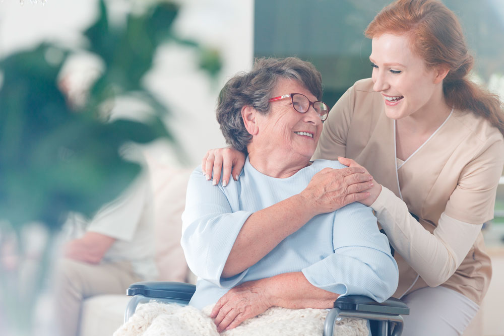 Lächelnde Seniorin im Pflegeheim bedankt sich bei einer Pflegerin