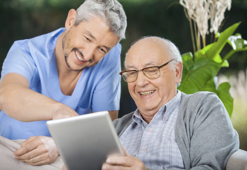 Ältere Person und Krankenschwester lächeln beim Blick auf ein Tablet